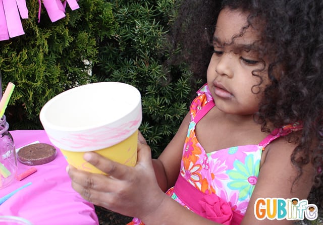 A lovely child at a vibrant kids’ party, happily decorating a clay pot with colourful paints.