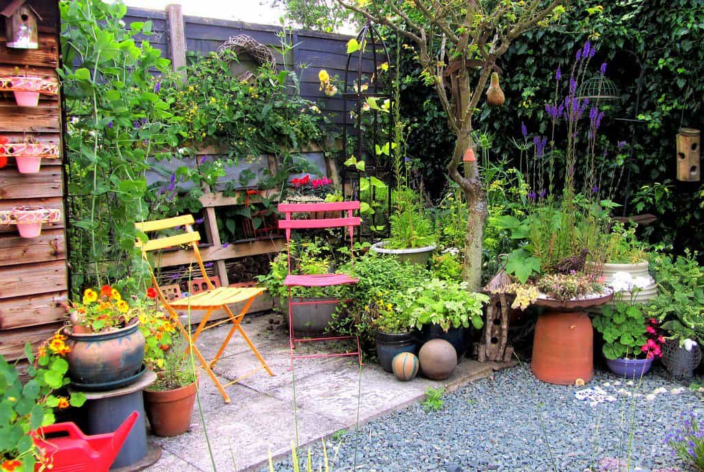 Corner back garden filled with lush green plants, showcasing vertical garden structures. Two vibrant bistro chairs in yellow and red add a pop of colour to the charming outdoor space.