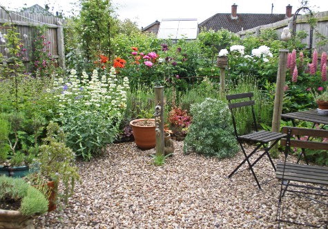 Small gravel garden adorned with diverse plants, featuring a cosy mini bistro set tucked in the corner.