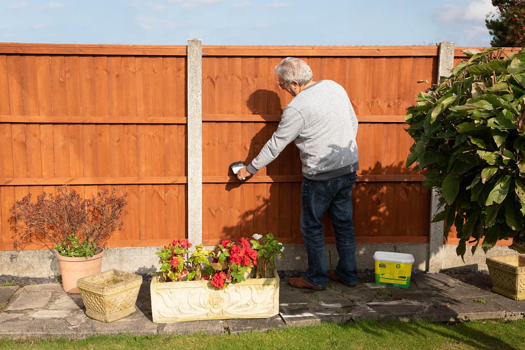 Man painting a garden fence, enhancing the outdoor space with a fresh coat of paint.