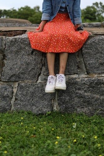 woman in an orange dress and denim jacket sitting on a stone wall