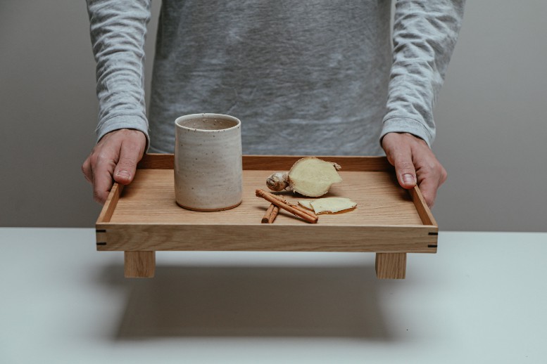 A person holding a wooden serving tray with a cup and herbs