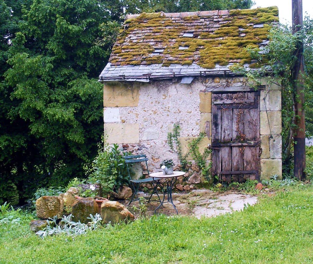 Stone garden shed with wooden door and algae-filled roof