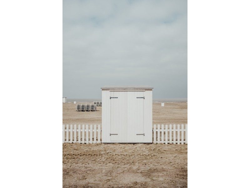 wooden shed on a beach against a small white picket fence