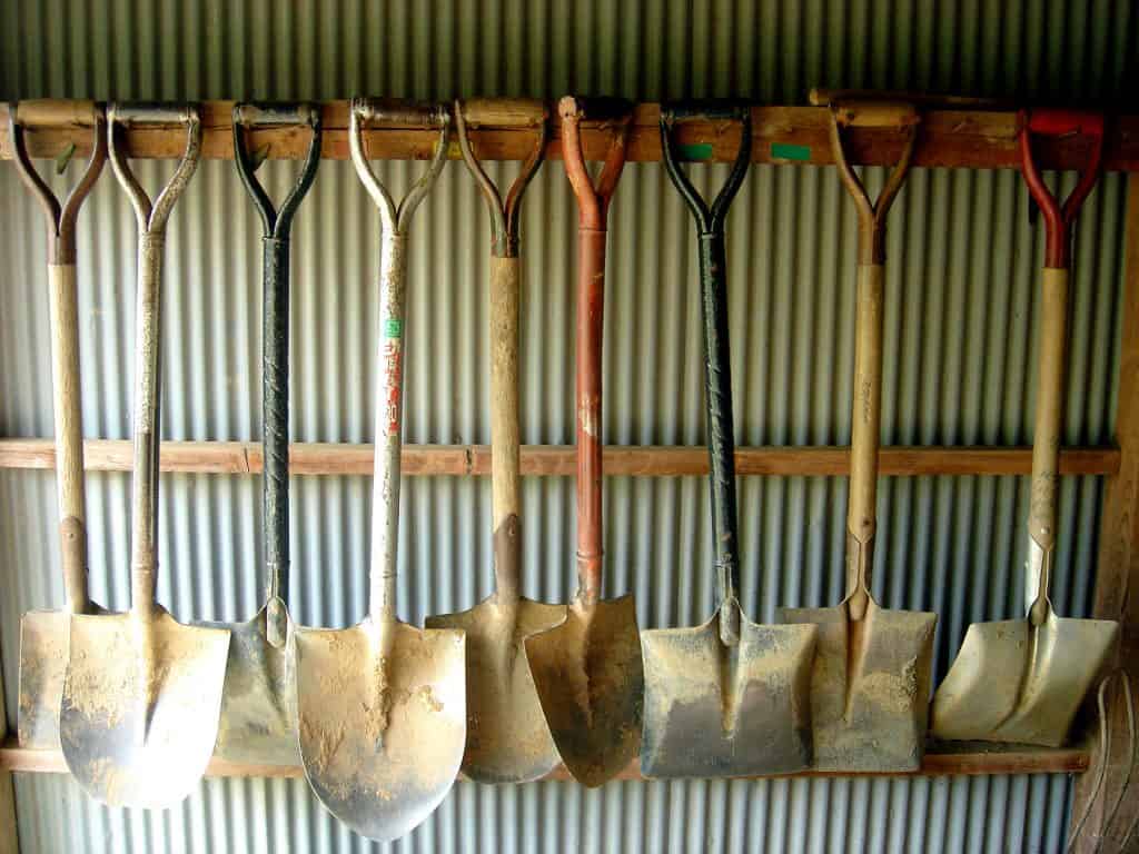 A collection of shovels hang on a wall hook