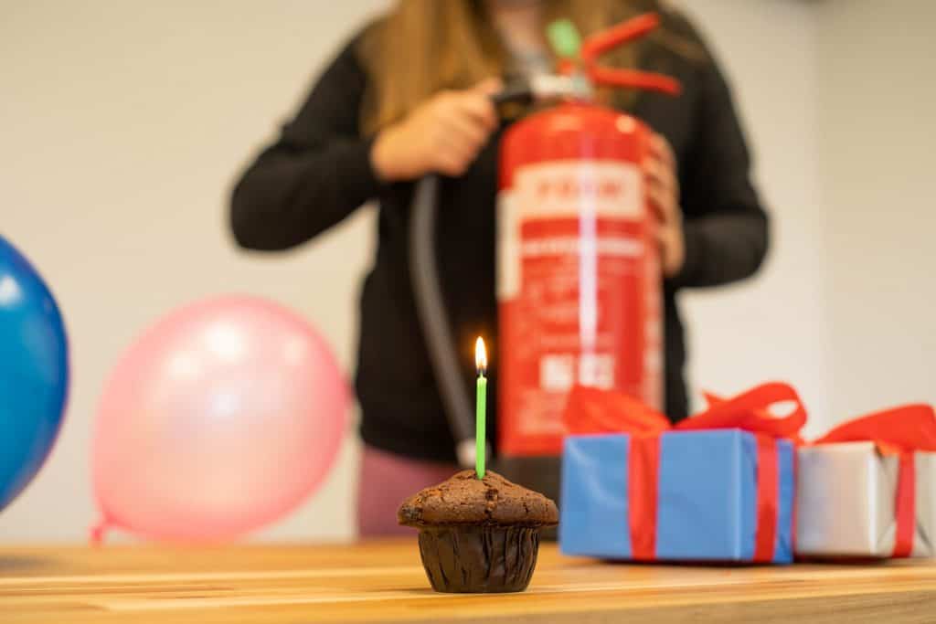 A cupcake with a birthday candle and a woman holding a fire extinguisher behind