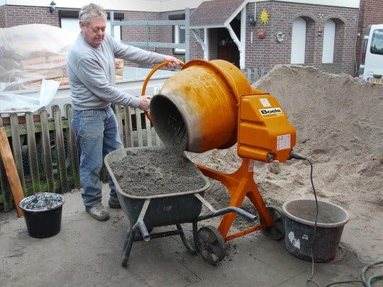 Man stood at cement mixer tipping it into wheelbarrow