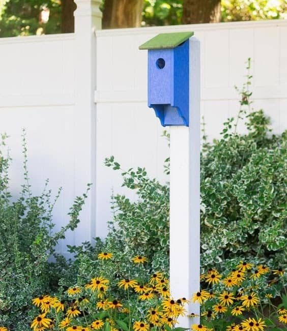 blue and green birdhouse on a white fence post with white fence in background