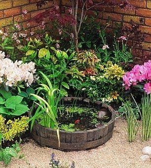 circular wood pond with flowers in the corner of two brick walls