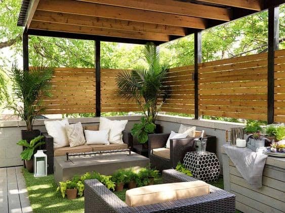 a garden with some rattan chairs, a coffee table, fake grass and a corner style pergola with some woven wood design and light still being allowed through.