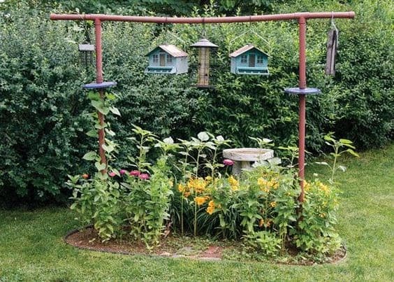 hanging bird feeders and houses from frame with tall plants underneath