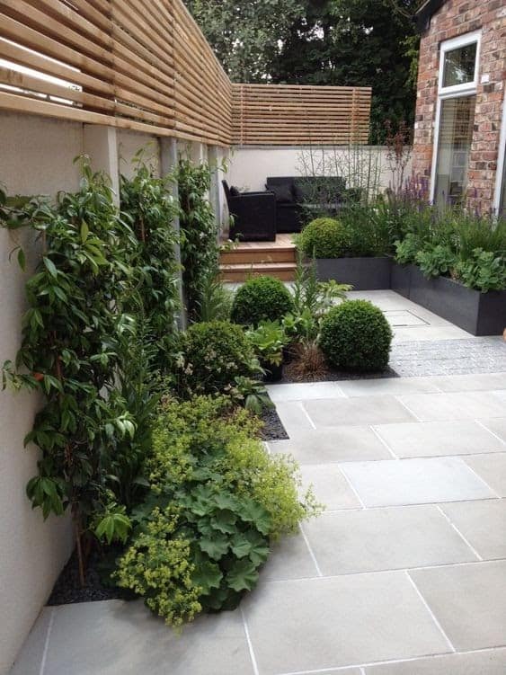 fencing above white stone walls covered in climbing plants and moss on a stone patio in a posh garden