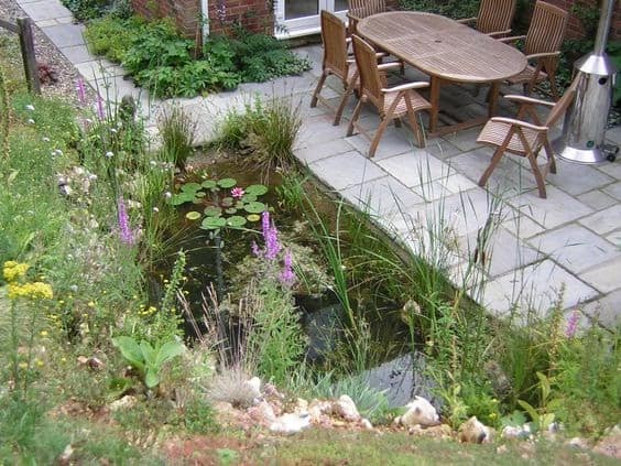 small pond next to patio with wooden garden furniture