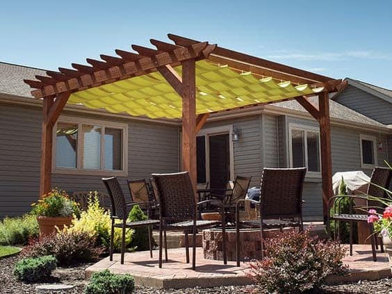 yellow tarpaulin/cloth/material suspended high off the ground on a large wooden pergola, covering a table and chairs outside a large house