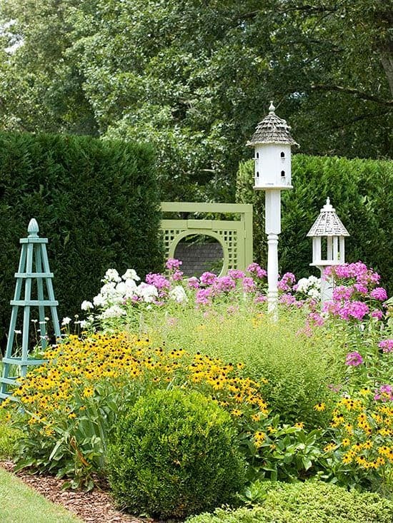 birdhouses coming out of tall flowers backed by hedges