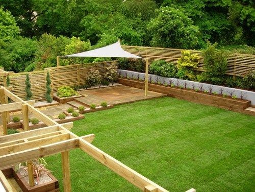 a triangular sail canopy in the corner of a garden covering some decking and creating shade