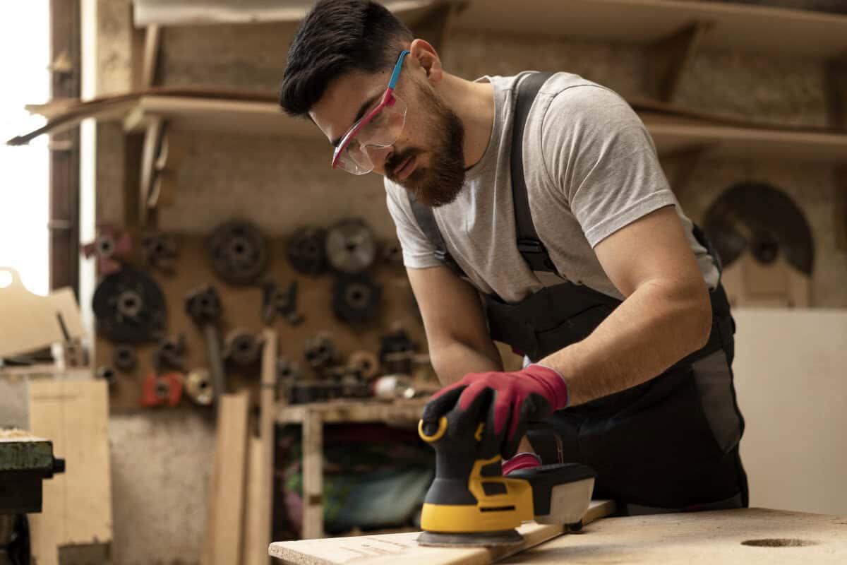 Man with safety glasses and gloves working on a woodworking project.