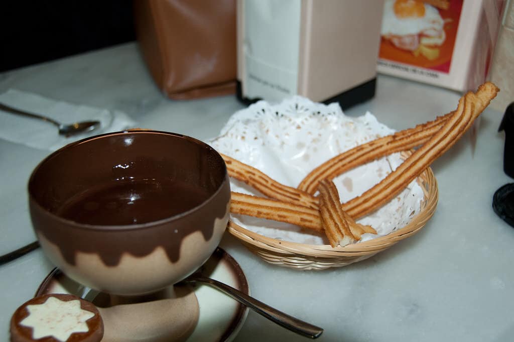 Hot chocolate and churros topped with whipped cream on a plate.