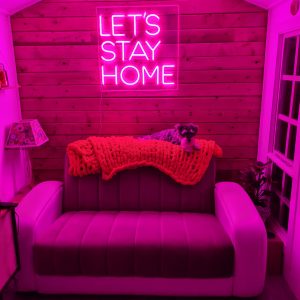 Summerhouse interior with comfy sofa and pink neon "let's stay home" sign
