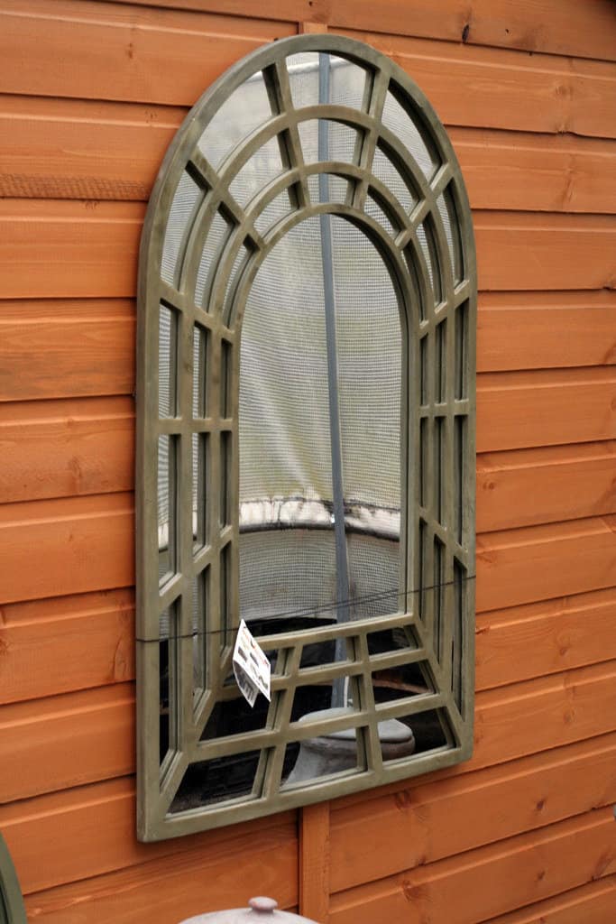 Arched window-style mirror adorned on a garden wall.