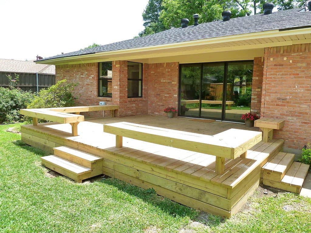 DIY wooden deck with built-in bench in contrast with red brick wall