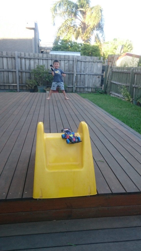 A kid jumping his remote controlled car over a baby slide on the deck