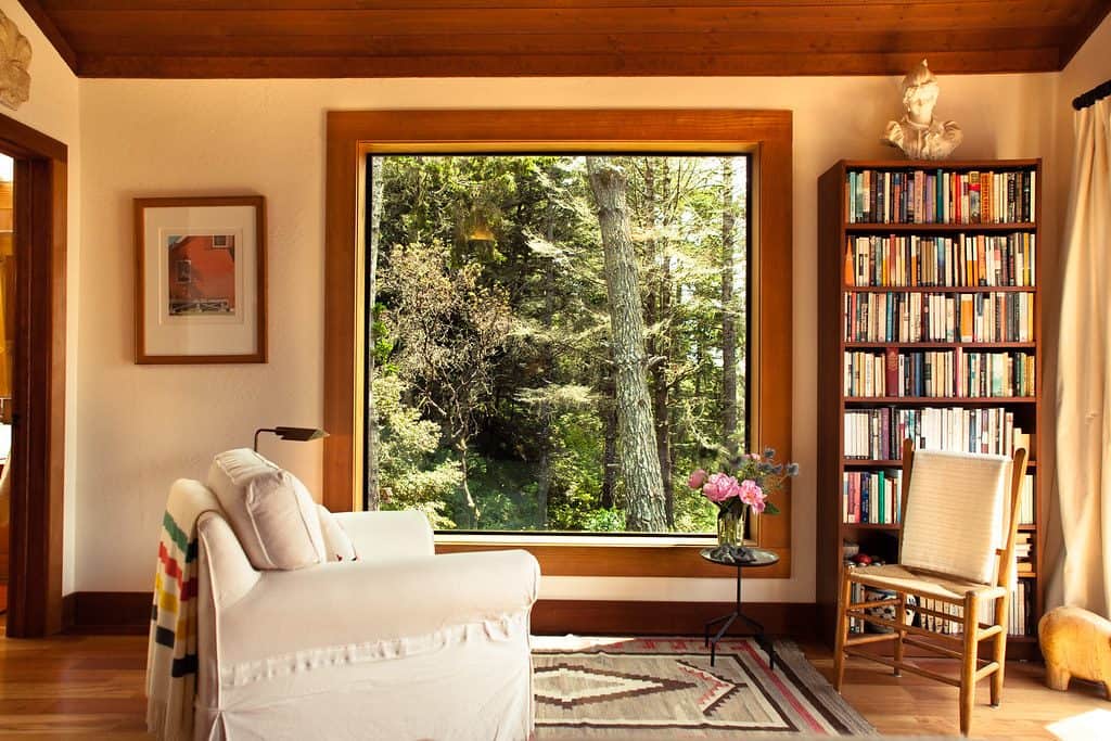 Bedroom's reading nook with bookshelf, seating area, and a glass window with forest view