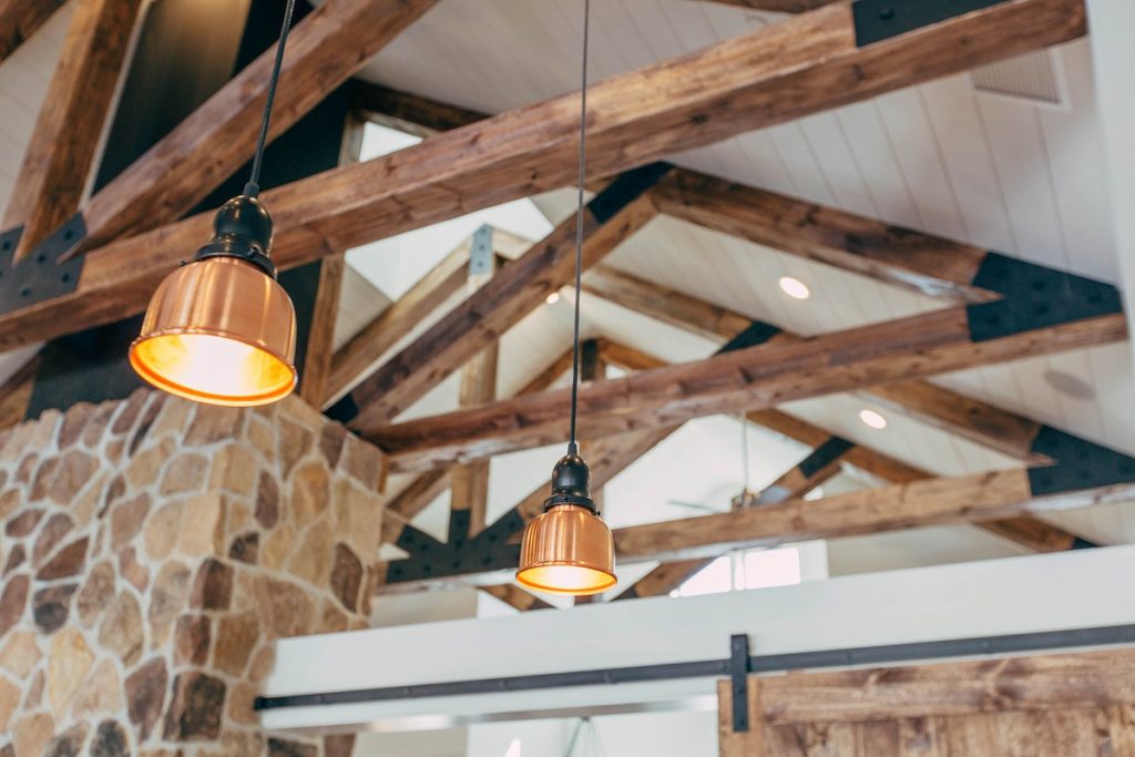 Ceiling of a house with wooden beams and rafters exposed and hanging lights between the rafters