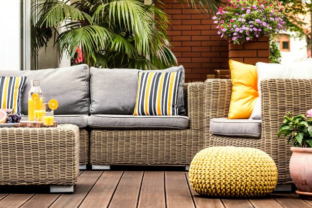 Yellow pouf next to rattan armchair on wooden terrace with striped pillows on sofa
