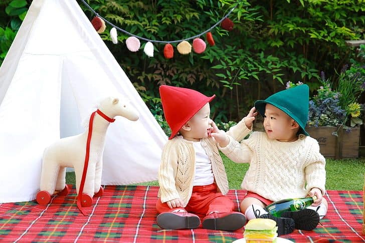 Two toddlers on a picnic blanket with a small teepee in the background