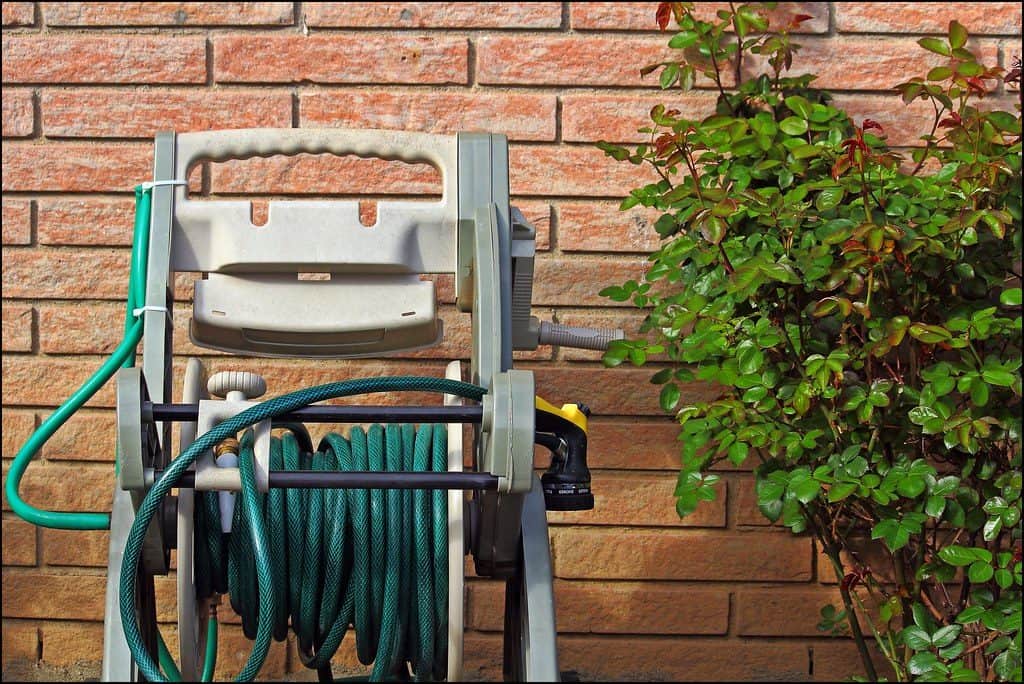 A garden hose tied up on a hose holder.