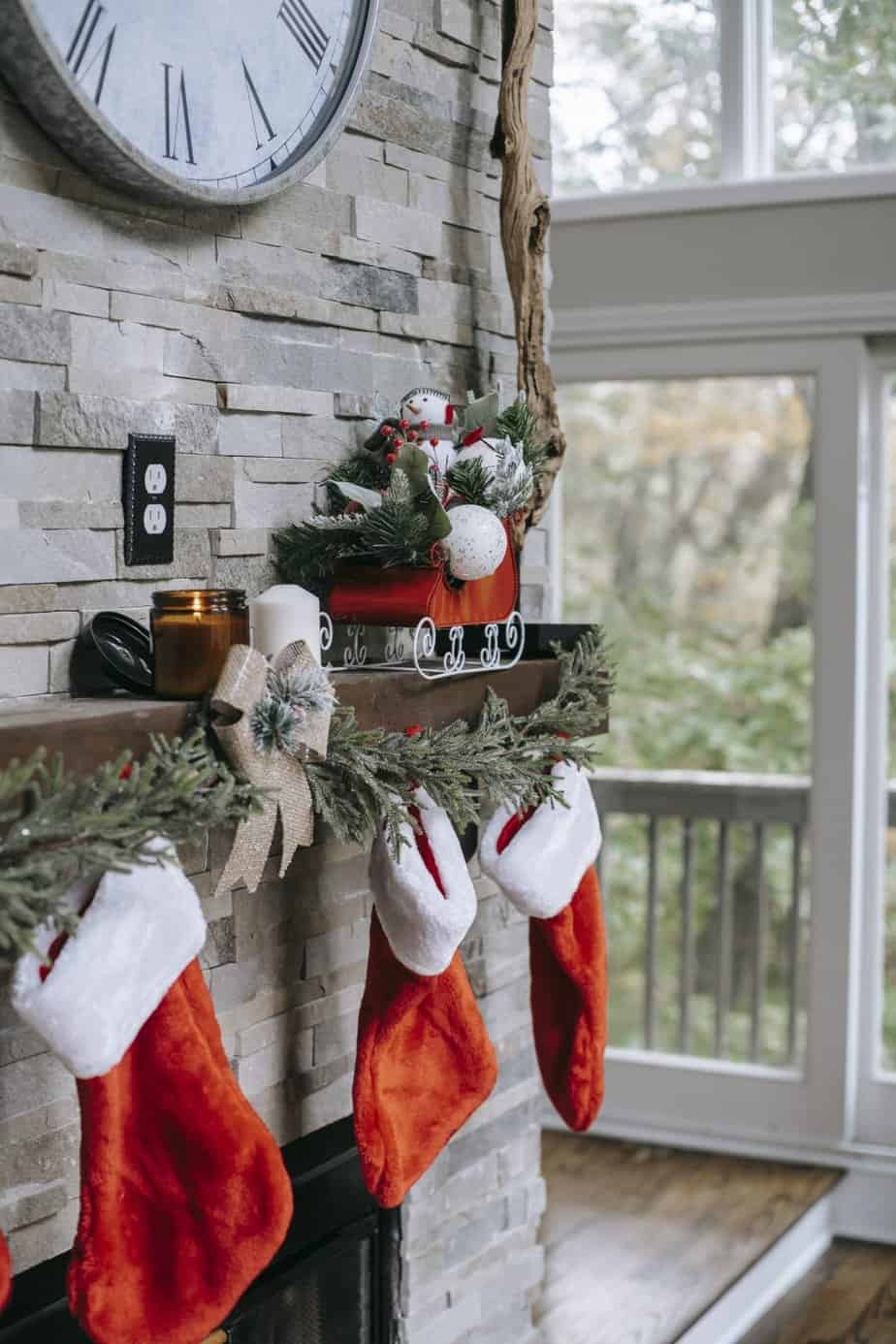 Modern stone fireplace mantel decorated with Christmas ornaments, stockings and pine cones