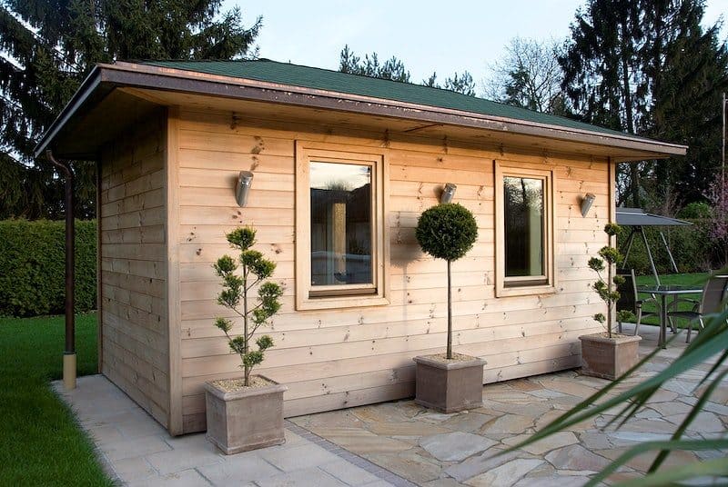 Modern log cabin exterior with potted trees and plants