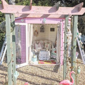 Pink summerhouse in a gravel garden framed by a pergola