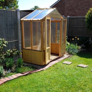 A wooden greenhouse under construction in a sunny garden.