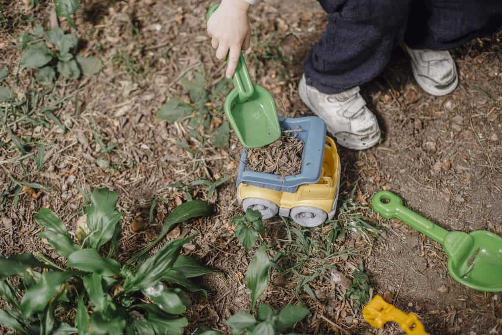 A kid holding a small toy shovel and a trucktor 