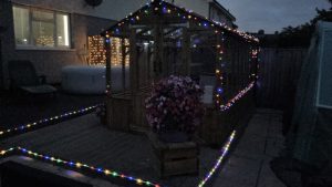 Wooden greenhouse covered in multi-coloured lights at nighttime
