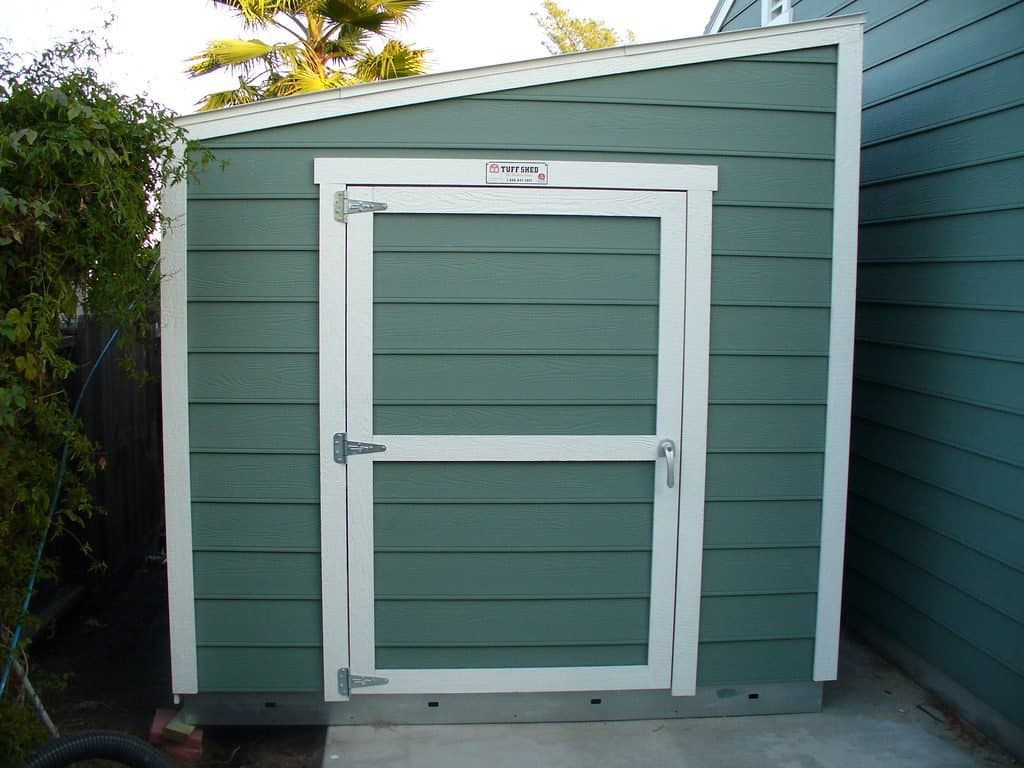 Green lean-to garden shed leaning against the house wall