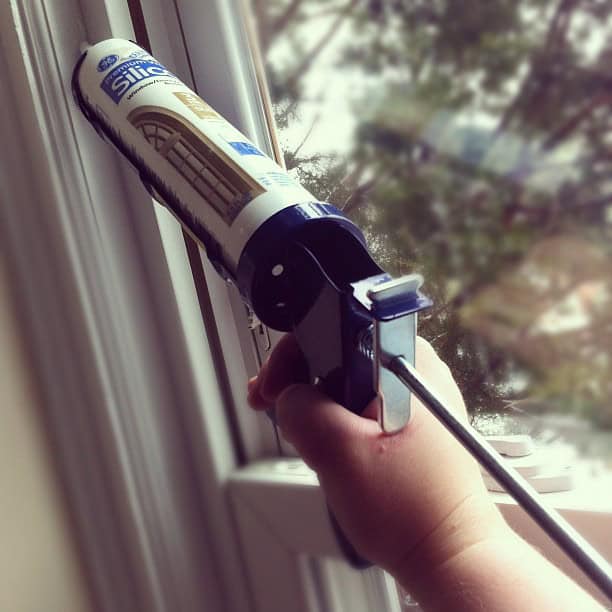 A person using a silicone caulk gun around a window.