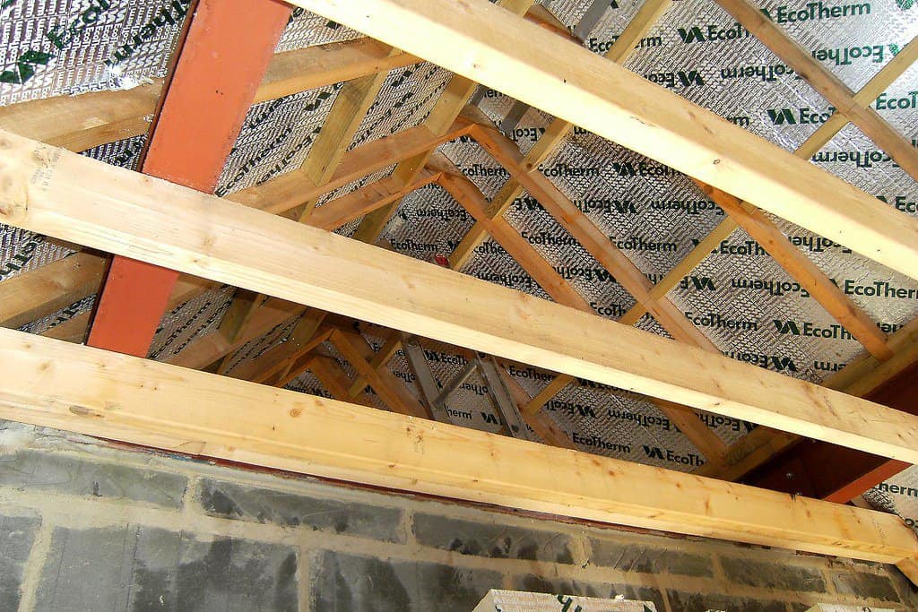 Bare roof ceiling with wooden beams and insulation material.