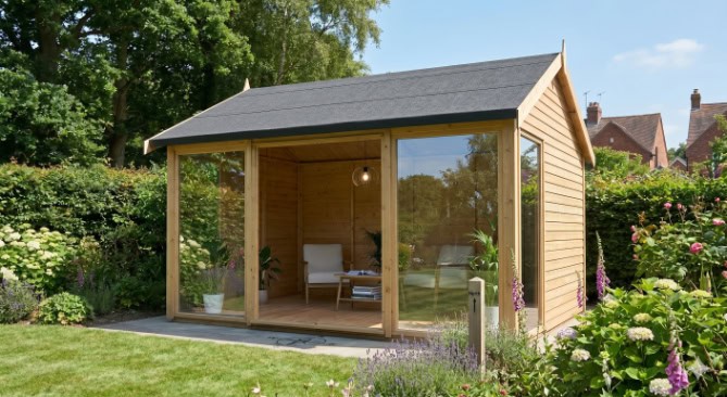 A summerhouse with floor-to-ceiling glass windows and doors facing north in a lush home garden.