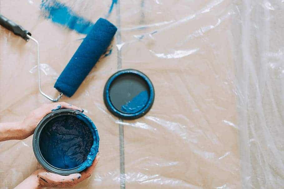 A person holding a blue paint can beside a blue roller brush