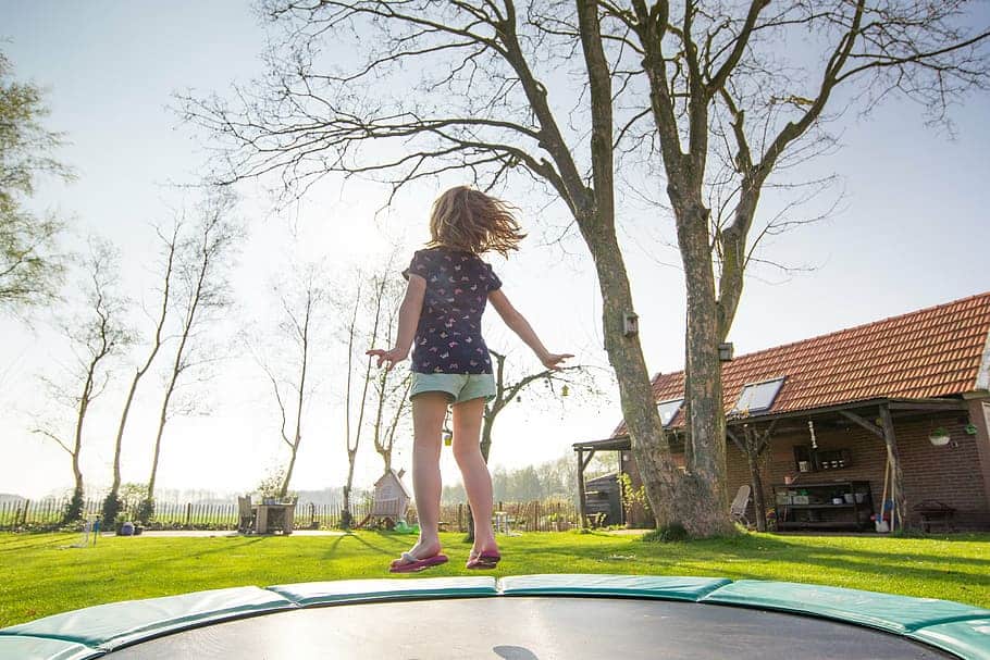 A kid jumping on a trampoline in the garden