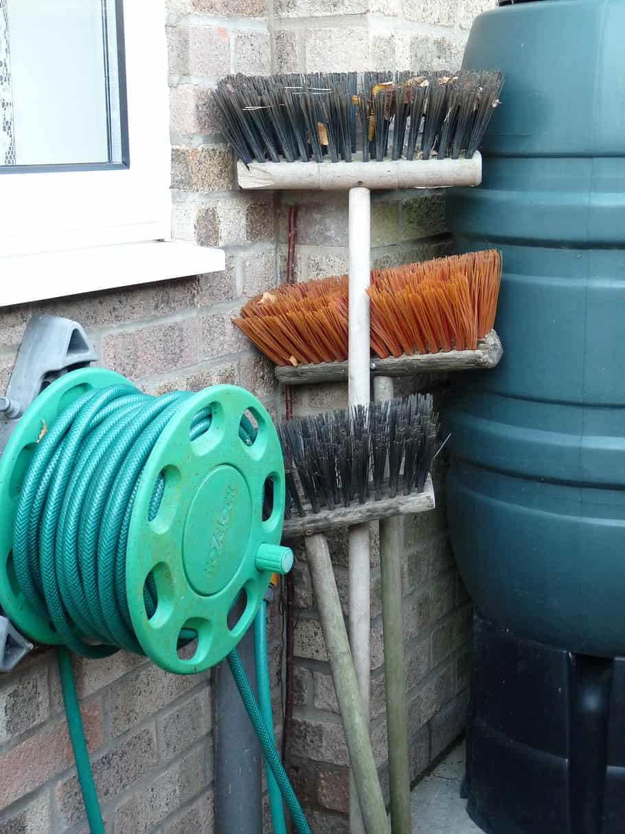 A broom and a garden hose pipe with a few brushes kept at the corner
