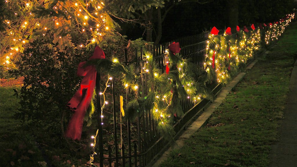 Festive garden fence adorned with sparkling Christmas lights, elegant garlands, and festive red bows.