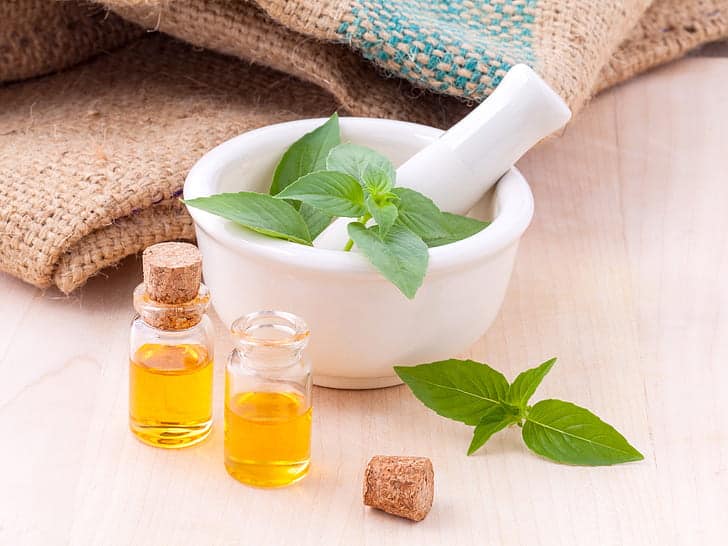 Fresh peppermint leaves in a porcelain mortar and pestle, surrounded by two bottles of essential oils.