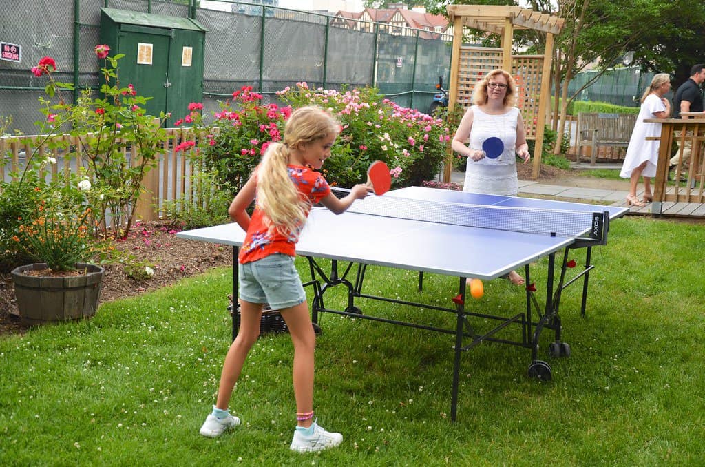 A girl and a woman are playing table tennis on a blue table in a garden.