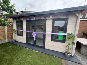 A completed garden log cabin, decorated with bunting and a purple opening ceremony ribbon