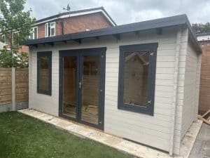 White log cabin in a residential garden with dark grey fascia and frames