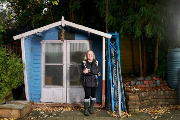 A woman in a jacket standing in front of a blue shed.